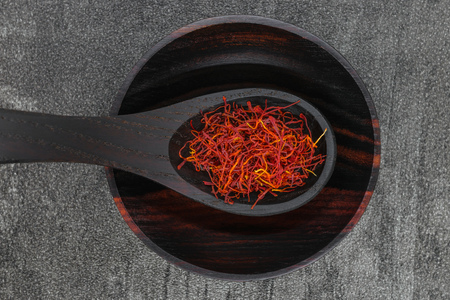 Saffron spices in black wooden spoon and bowl on black stone backgroundの写真素材