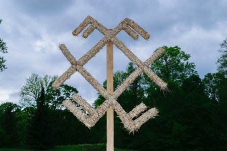 Baltic mythology gods symbol made from straws standing in the green meadow and dense and dark forest during cloudy dayの写真素材