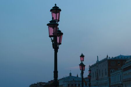 Authentic pink Venice street lanterns in the background of late summer evening, buildings, blue sky and flying seagulls in Venice, Italyの写真素材