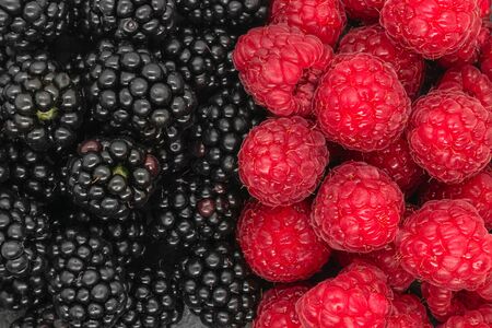 Background of blackberries and raspberries on black stone background. Area divided in the half of two type of berriesの写真素材