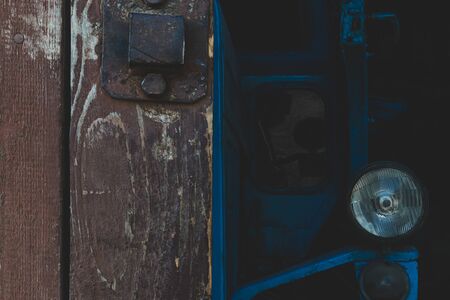 Abstract composition of the half of rural brown barn gate door and part of standing very old blue tractor. Tractor and doors are in camera focusの写真素材