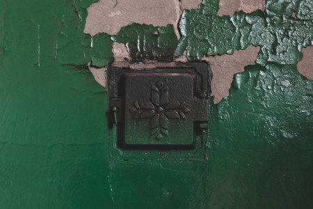 Concrete rural stove with closed metal doors and peeling green paints from the wall
