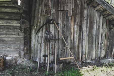 Very old, rusty and dirty garden working rural tools (hoe, scythe, spade, rake, ax, pitchfork) near the barn wooden wall in countryside during summer timeの写真素材
