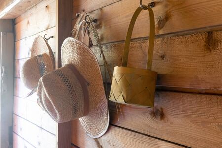 Straw hats, rye bouquet and wooden basket hanging on wooden wall of countryside house and illuminated by sun beamsの写真素材