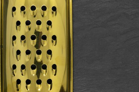 Part of golden and shiny hand grater with holes on black stone background with copy spaceの写真素材