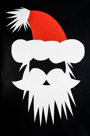 Abstract composition of Santa Claus head with cap made of white nd red paper and placed on dark black and grey background with copy spaceの写真素材
