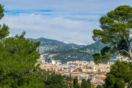 Landscape view of Nice city buildings, green trees and snowy mountains during clear and sunny day in the background of blue sky with the cloudsの写真素材