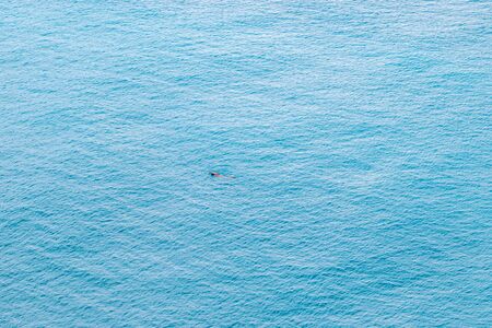 Aerial view of lonely swimmer swimming in the calm and blue seaの写真素材