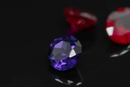 Macro view of round purple amethyst gemstone on black reflective surface with two blurred red rubies...