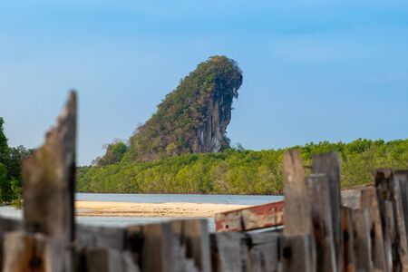 Very old and abandoned wooden boat in front of the Khao Khanab Nam mountains, mangroves forest and blue sky with rain clouds in Krabi town, Thailand. Mountains is in camera focusの写真素材