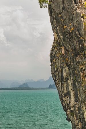 Authentic landscape view with copy space of big cliff in foreground and mountains, green gulf sea water in the background during hot and cloudy day in Thailandの写真素材