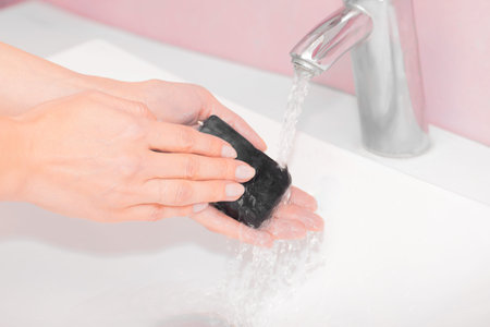 Healthcare concept. Close-up view of woman washing hands with black soap over sink in bathroom