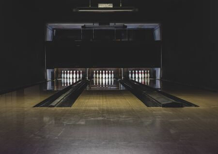 Leisure, entertainment and activities concept. Abstract background with copy space of old and dark parquet bowling track with white pins at the end of it. Floor in the center is in camera focusの写真素材