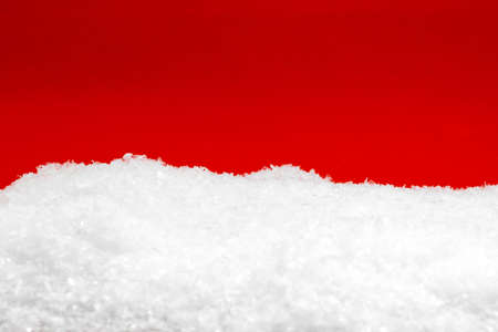 Christmas and holidays concept. Artificial snow in red background with copy space. Snow near red background is in camera focusの写真素材