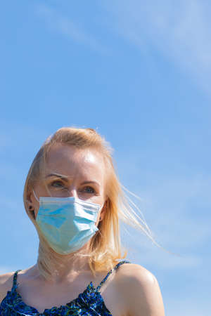 Healthcare and medicine concept. Portrait of blonde woman with windswept hair and medicine mask on her face. Woman wear blue dress in blue sky background with copy spaceの写真素材