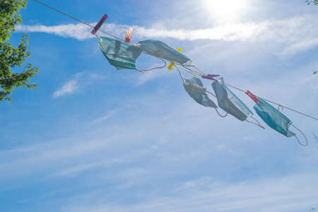 Healthcare and medicine concept. Used medicine face masks hanging like laundry on rope and fixed with colorful laundry pins in front of the blue and sunny sky with copy spaceの写真素材