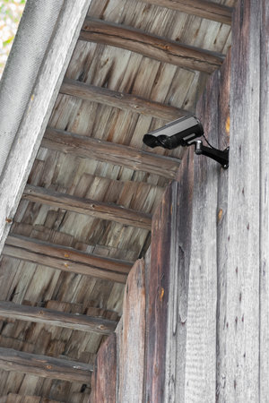Home protection concept. Black CCTV camera attached on wooden barn wall under roof with copy space