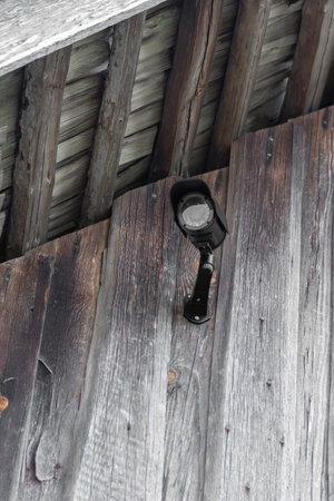 Home protection concept. Black CCTV camera attached on wooden barn wall under roof with copy space