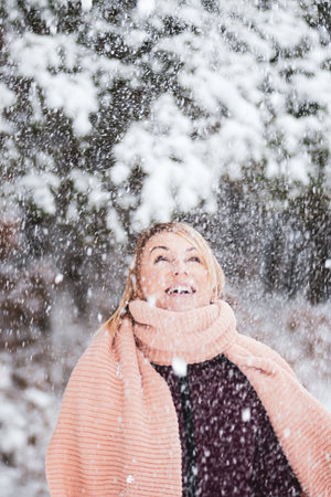 Blonde woman with purple coat and pink scarf enjoys of heavy snowing and blizzard during winter time in forest backgroundの写真素材