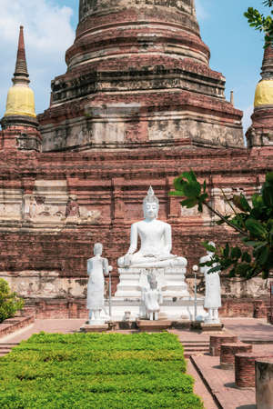 Red bricks Wat Yai Chai Mongkhon ancient temple with green bushes park and white sitting buddha in Bangkok, Thailand during sunny and hot dayの写真素材