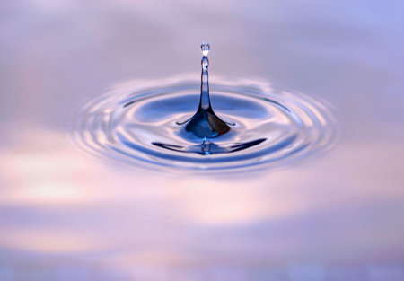 Water droplet dripping into blue and purple pool creating ripples and abstract shape of water....