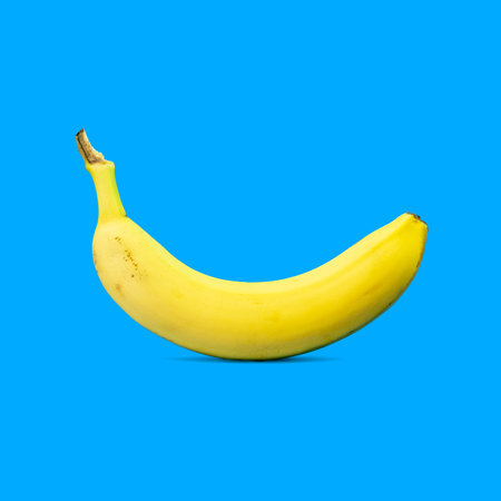 Minimal summer food concept. Yellow banana fruit casting shadow on blue vivid background with copy space