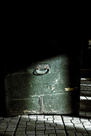 Very old, aged and grunge green wooden chest with rusty steel frames and handle in dark background and part of it illuminated by sun beam and another part is in shadow. HDR imageの写真素材