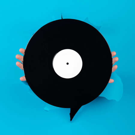 Music, entertainment, technology, retro, vintage concept. Woman hands holding black and blank vinyl record on torn blue paper background with copy spaceの写真素材