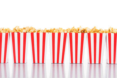 Cinema, movie and theater concept. Popcorn boxes with white and red stripes full of sweet with caramel popcorn on white reflective background in white background with copy spaceの写真素材