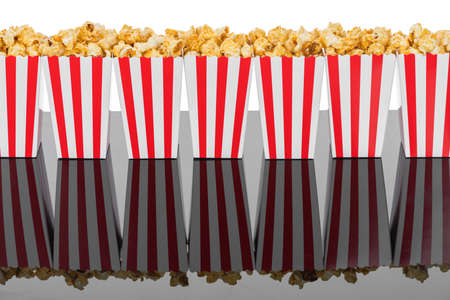 Cinema, movie and theater concept. Popcorn boxes with white and red stripes full of sweet with caramel popcorn on black reflective background in white background with copy spaceの写真素材