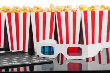 Cinema, movie, leisure and theater concept. Popcorn boxes with white and red stripes full of sweet with caramel popcorn, 3D glasses and clapperboard on black reflective backgroundの写真素材
