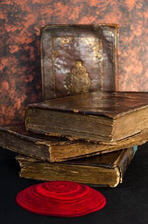 A stack of old leather-bound Jewish books with gold stamping and red knitted jewish bale on black background. Closeupの写真素材