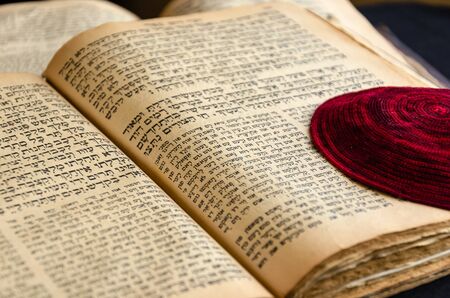 An open old Jewish book. Red knitted jewish bale lies on an open scripture page. Hebrew text. Selective focus. Closeupの写真素材