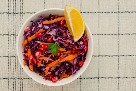 Red cabbage coleslaw with carrots, pomegranate and slice of lemon in a white bowl on a linen background. Healthy vegetarian and vegan food. Low calorie diet conceptの写真素材