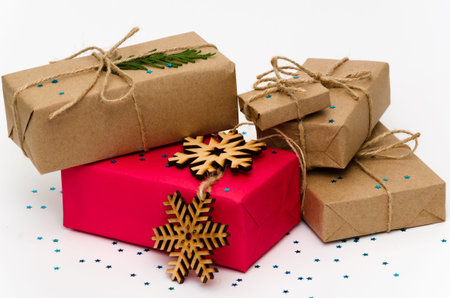 Pile of gift boxes wrapped in kraft brown paper and one in pink on a white background adorned with...