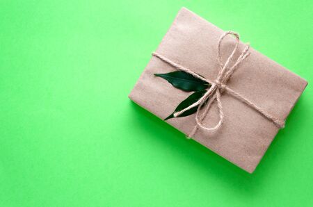 Gift box wrapped in kraft paper tied with twine and decorated with two green leaves on a light green background. DIY present idea. Zero waste holidays concept. Flat lay. Copy spaceの写真素材