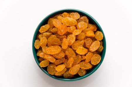 White or golden raisins in a blue ceramic bowl on a white background. Healthy sweets concept. Close-up. Top viewの写真素材