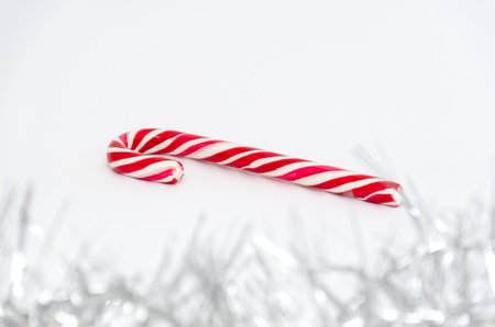 Classic glossy red and white christmas candy cane on white background. Garland in the foreground....