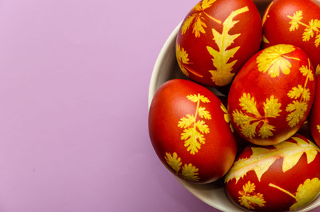 Easter eggs dyed with onion peels with a pattern of fresh leaves of plants in a white bowl on a...