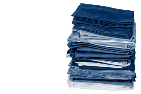 Stack of folded clean blue bedding on a white background: duvet covers, sheets, pillowcases. The...