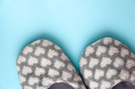Pair of gray fluffy slippers with white hearts on light blue background. Warm cozy home footwear. Rest at home, relaxation, coziness, hygge concept. Close-up. Top view, copy spaceの写真素材