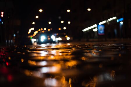 Wet paving stones on the roadway. Glare from night illumination. Rainy evening in the city. View from sidewalk level. Soft focusの写真素材