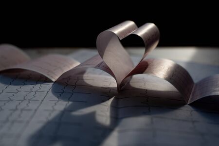 Heart shape made of cardiogram printout in the dark. Cardiovascular diseases and heart check concept. Medical background. Closeupの写真素材