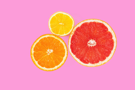 Halves of orange, pink grapefruit and lemon on pink background. Top view of cross section of citrus fruits. Minimal composition. Close-upの写真素材