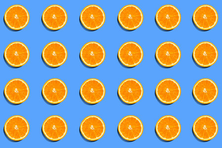 Summer pattern of fresh orange slices on blue background. Top view of cross section of colorful citrus fruit. Contrasting flat lay compositionの写真素材