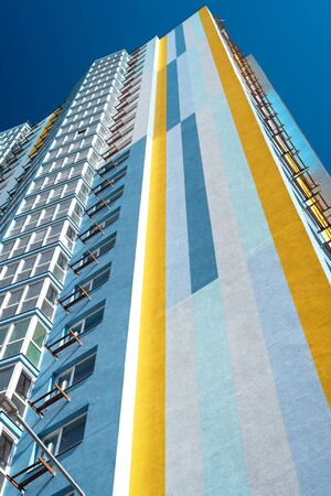 Modern multi-storey residential building against blue sky on sunny day. Exterior wall of multicolored high-rise house. View from below. Vertical orientationの写真素材