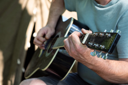 Man playing classical acoustic guitar sitting near tent outdoors. Closeup of hands. Selective focus....