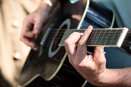 Closeup of man's hands playing acoustic guitar sitting near tent outdoors. Selective focus. Romance...