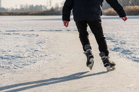 Skater legs at skating rink. Man skating on white ice on frozen lake. Back view. Winter leisure activityの写真素材