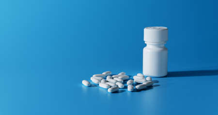 Medical white bottle and pills on blue background. Banner. Copy space. Selective focusの写真素材